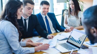 Team of professionals reviewing financial charts around a laptop with bar and line graphs in a bright conference room